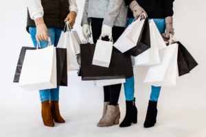 We can see the feet and legs of three women dressed in jeans and boots, carrying bags of gifts.