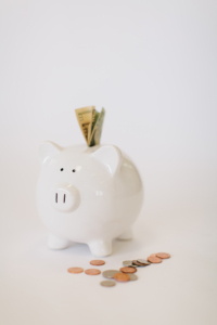 In the image we can see a savings pig overflowing with money on a white background, and some coins on the table.