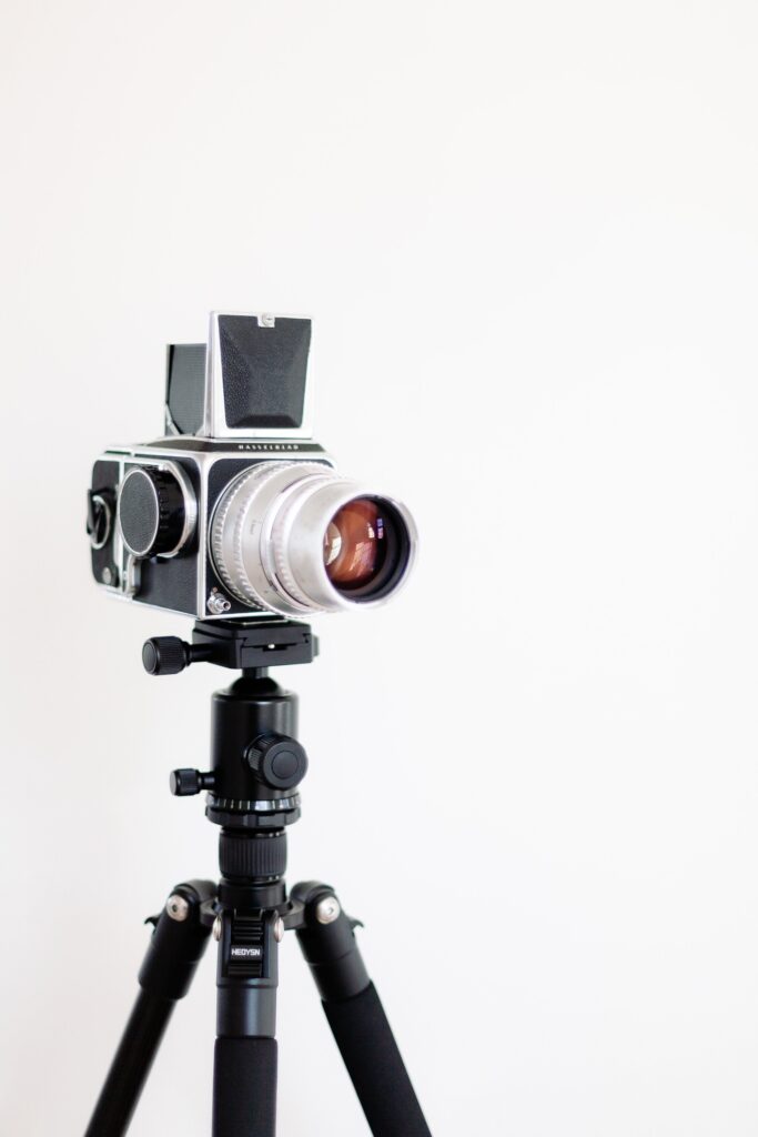 We can see a professional camera placed on its support, behind, a white background.